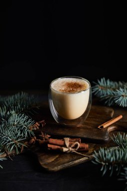Kesme tahtasında aromalı eggnog kokteyli, tarçın çubukları ve siyah üzerine ayrılmış ladin dalları.