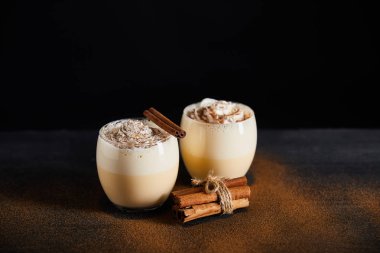 Krem şantili ve tarçın çubuklu geleneksel eggnog kokteyli. Masanın üzerinde siyah izole edilmiş tarçın tozu var.