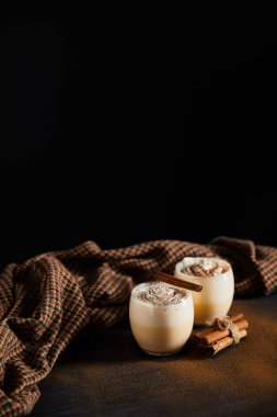 Krem şantili eggnog kokteyli, tarçın çubukları ve siyah üzerine izole edilmiş tarçın tozu kaplı kareli kumaş.