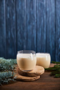 Lezzetli eggnog kokteyli yuvarlak ahşap tahtalar üzerinde ladin dallarının yanında mavi desenli arka planda. 