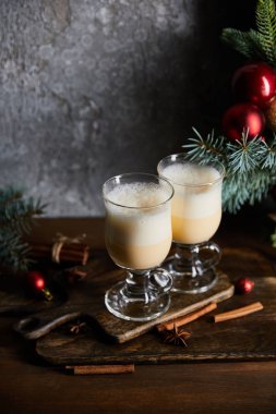 Gri taş arka planda süslü ladin dallarının yanındaki kesme tahtasındaki geleneksel eggnog kokteyli.