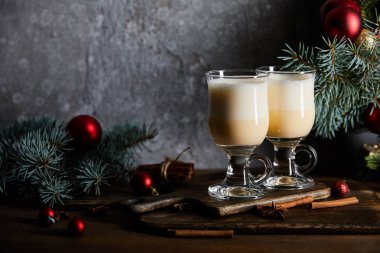 Gri taş arka planda süslü ladin dallarının yanındaki kesme tahtasındaki geleneksel eggnog kokteyli.