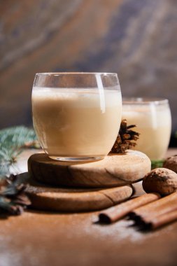 Yuvarlak tahtalarda nefis eggnog kokteylinin seçici odak noktası, ladin konileri, tarçın çubukları ve mermer taşlı arka planda cevizler