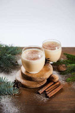 Yuvarlak tahtalarda aromalı eggnog kokteyli, ladin dalları, tarçın çubukları ve gri üzerine izole edilmiş cevizler.