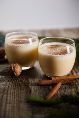 Tarçın çubuklarının yanında aromalı eggnog kokteylinin seçici odak noktası ve ahşap masa üzerinde izole edilmiş ceviz.