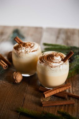 Tarçın çubuklarının yanında krem şantili nefis bir eggnog kokteyli ve ahşap masada yalıtılmış cevizler.
