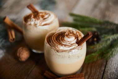 Tarçın çubuklarının yanında krem şantili eggnog kokteyli, ladin dalı ve ahşap masada ceviz.