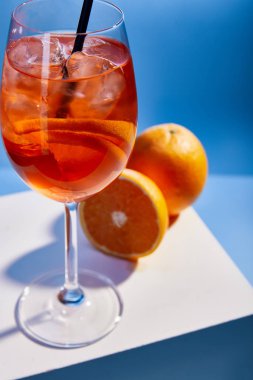 selective focus of cocktail Aperol Spritz with straw in glass and oranges on blue background  clipart