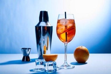 Kokteyl Aperol Spritz, portakal, karıştırıcı, buz küpleri ve mavi arkaplanda ölçü kabı. 