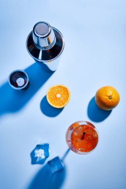 Kokteyl Aperol Spritz 'in üst görünümü, portakallar, titretici, buz küpleri ve mavi arkaplanda ölçüm kabı 