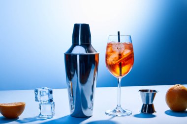 Kokteyl Aperol Spritz, portakal, karıştırıcı, buz küpleri ve mavi arkaplanda ölçü kabı. 
