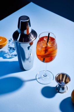 high angle view of cocktail Aperol Spritz, orange, shaker, ice cubes and measuring cup on blue background  clipart