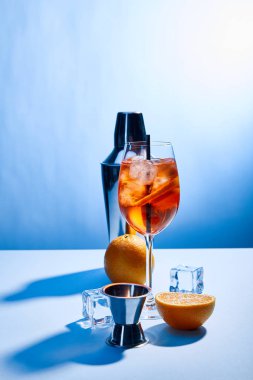 cocktail Aperol Spritz, oranges, shaker, ice cubes and measuring cup on blue background  clipart