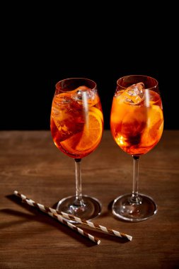 Aperol Spritz bardaklarda ve tahta masada pipetlerle 