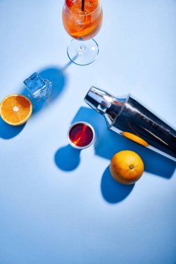 top view of Aperol Spritz, oranges, shaker, ice cubes and measuring cup on blue background  clipart