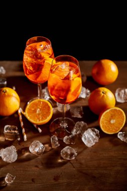 high angle view of Aperol Spritz in glasses, oranges and ice cubes on black background  clipart