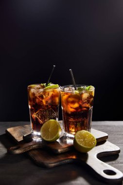 cocktails cuba libre in glasses with straws and limes on black background  clipart