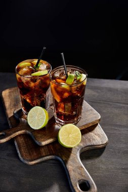 high angle view of cocktails cuba libre in glasses with straws and limes on black background  clipart
