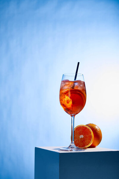 cocktail Aperol Spritz with straw in glass and oranges on blue background 