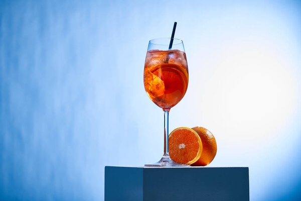 cocktail Aperol Spritz with straw in glass and oranges on blue background 