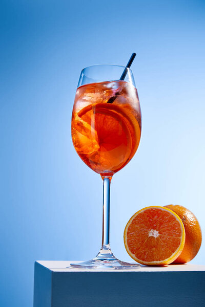 cocktail Aperol Spritz with straw in glass and oranges on blue background 