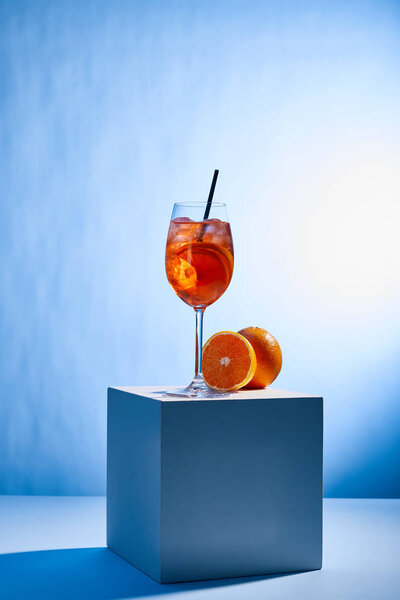 cocktail Aperol Spritz with straw in glass and oranges on blue background 