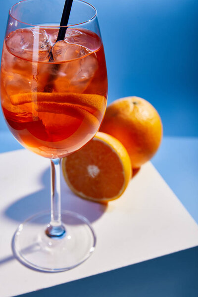 selective focus of cocktail Aperol Spritz with straw in glass and oranges on blue background 