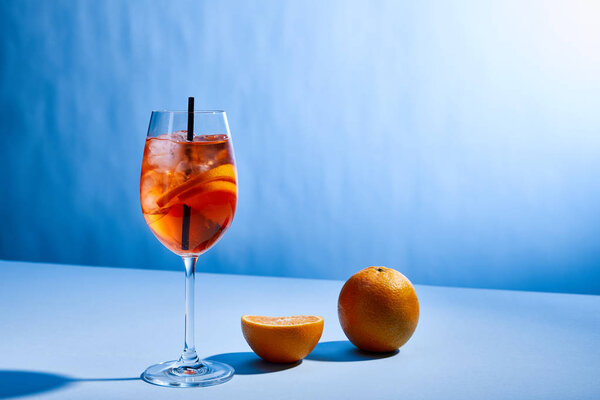 cocktail Aperol Spritz with straw in glass and oranges on blue background 