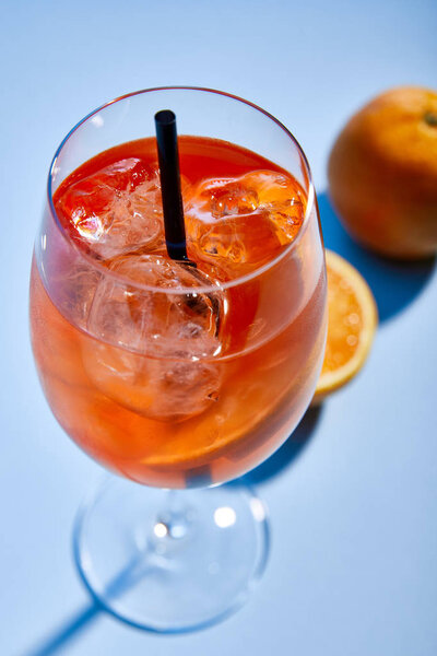 selective focus of cocktail Aperol Spritz with straw in glass and oranges on blue background 
