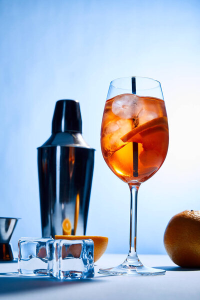 cocktail Aperol Spritz, oranges, shaker, ice cubes and measuring cup on blue background 