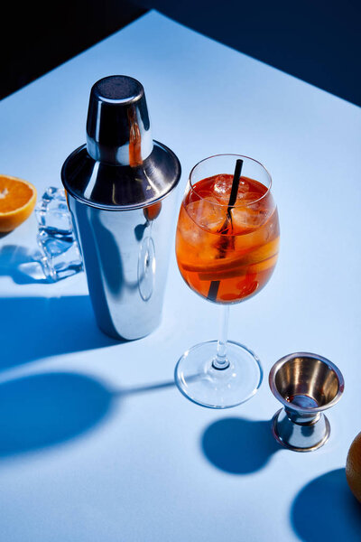 high angle view of cocktail Aperol Spritz, orange, shaker, ice cubes and measuring cup on blue background 