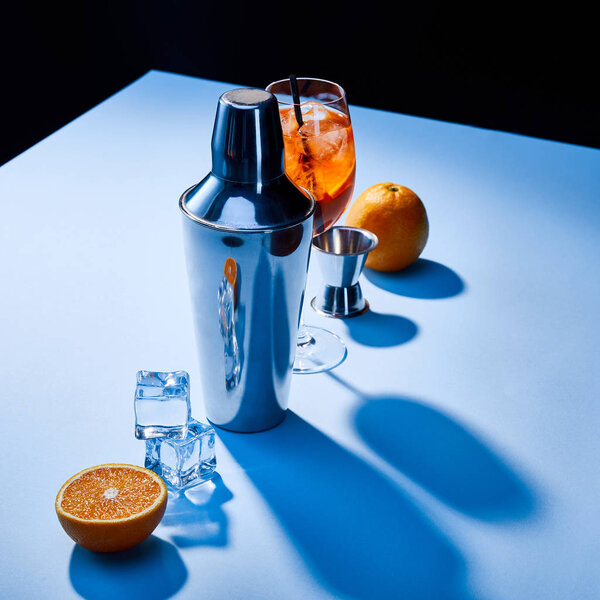 cocktail Aperol Spritz, oranges, shaker, ice cubes and measuring cup on blue background 
