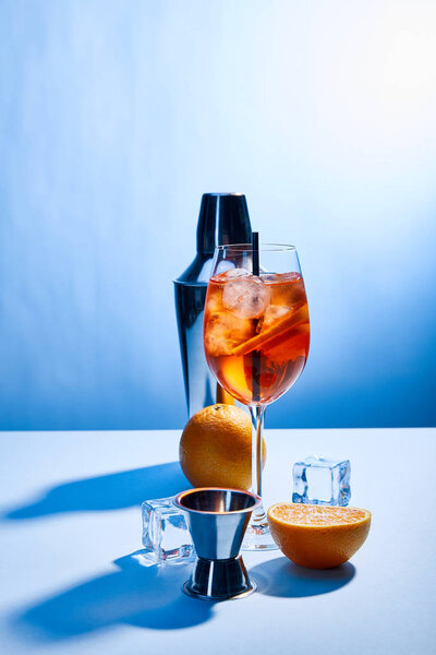 cocktail Aperol Spritz, oranges, shaker, ice cubes and measuring cup on blue background 