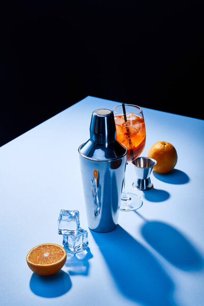 cocktail Aperol Spritz, oranges, shaker, ice cubes and measuring cup on blue background 