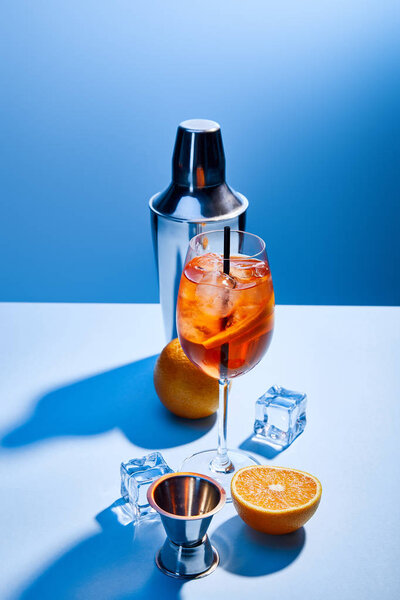 cocktail Aperol Spritz, oranges, shaker, ice cubes and measuring cup on blue background 