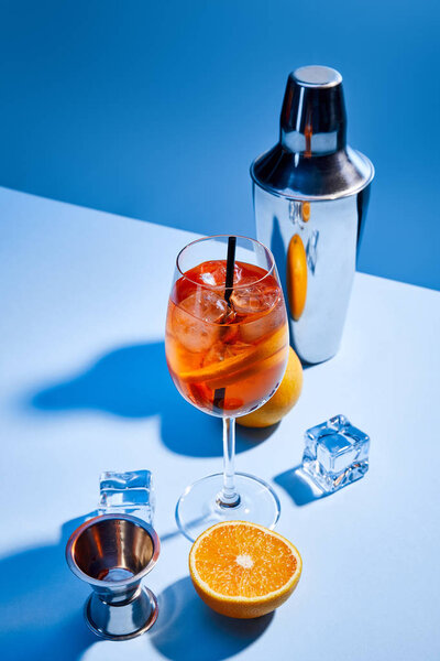cocktail Aperol Spritz, oranges, shaker, ice cubes and measuring cup on blue background 