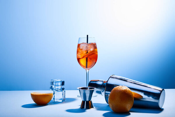 cocktail Aperol Spritz, oranges, shaker, ice cubes and measuring cup on blue background 