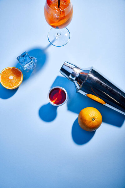 top view of Aperol Spritz, oranges, shaker, ice cubes and measuring cup on blue background 