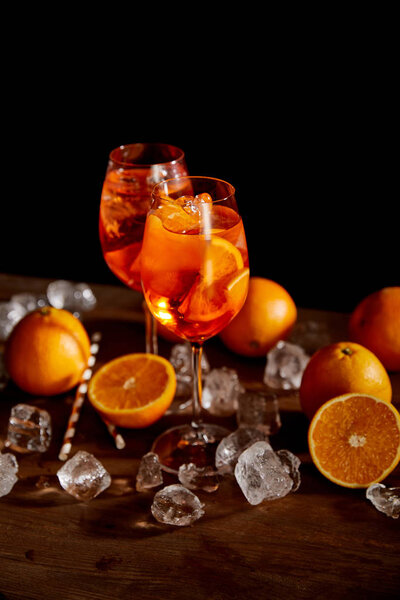 selective focus of Aperol Spritz in glasses, oranges and ice cubes on black background 
