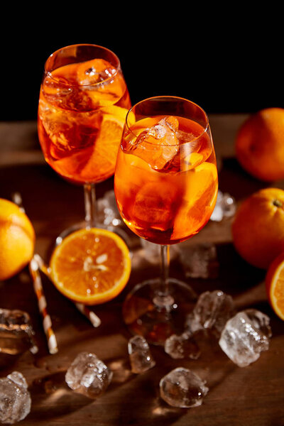selective focus of Aperol Spritz in glasses, oranges and ice cubes on black background 