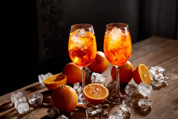Aperol Spritz в очках, апельсинах и кубиках льда на черном фоне
 