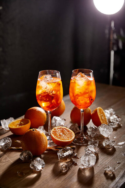 Aperol Spritz in glasses, oranges and ice cubes on black background 