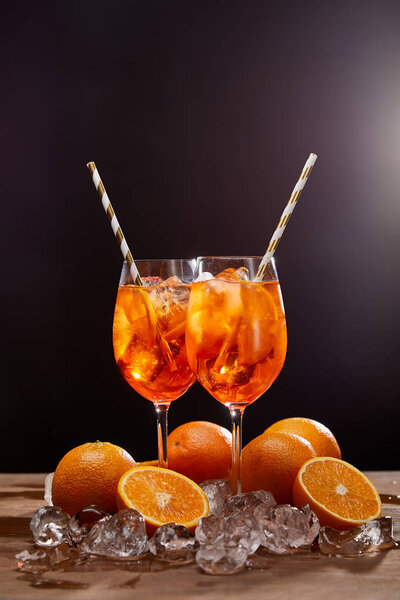 Aperol Spritz in glasses, oranges and ice cubes on black background 