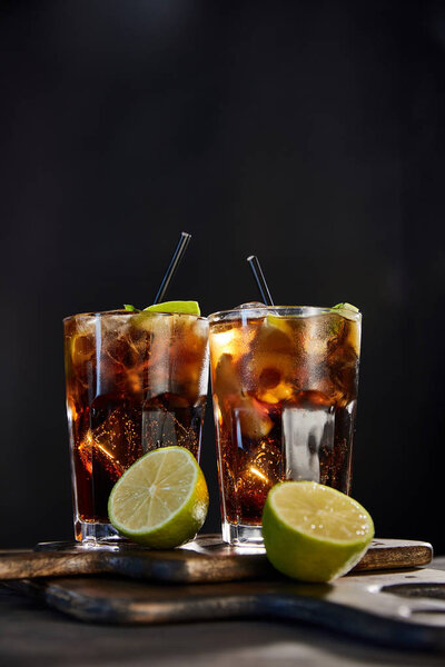 cocktails cuba libre in glasses with straws and limes on black background 