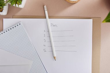 top view of green plants, envelope, blank notebook, pencils and paper with plan lettering on beige surface clipart