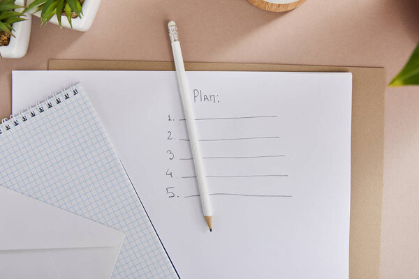 top view of green plants, envelope, blank notebook, pencils and paper with plan lettering on beige surface
