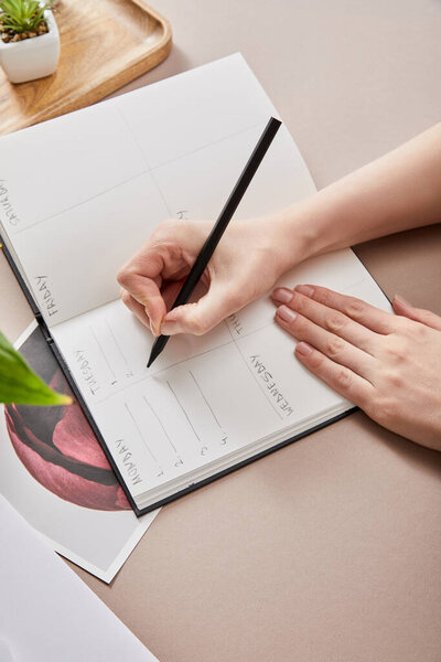 обрезанный вид женщины, пишущей в планировщике на бежевой поверхности
