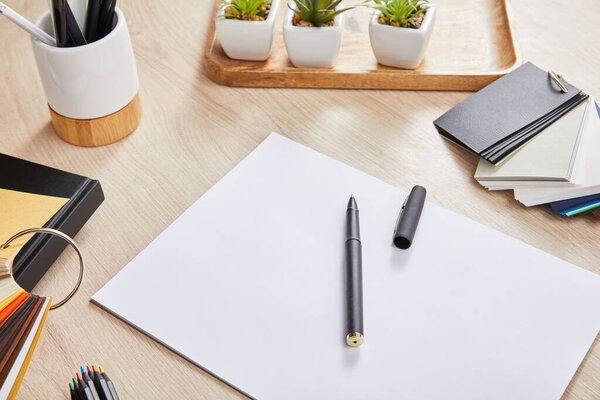 зеленые растения, цветные карандаши, цветовая палитра и белая бумага с ручкой на деревянной поверхности
