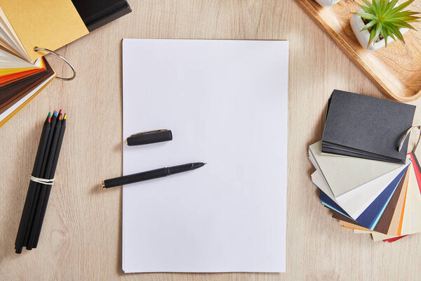 вид сверху на зеленые растения, цветные карандаши, цветовую палитру и белую бумагу с ручкой на деревянной поверхности
