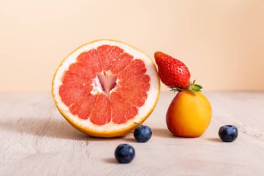 fruit composition with berries, grapefruit and apricot on wooden surface isolated on beige clipart